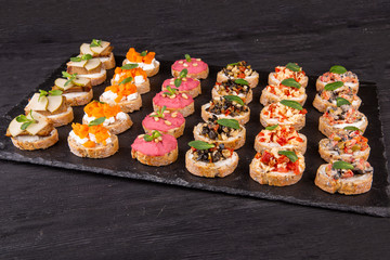 Assorty canape of toast with fish, meat and vegetables on a black background