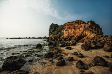 Ocean, sandy beach with large boulders, rock and flying bird. Sri Lanka.