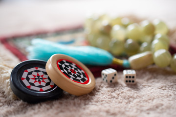 On a bright Mat are dice with numbers, a black and white patterned chip for backgammon and onyx rosary: a concept of Board games, macro, close up