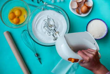 Meringue cookie recipe top view. Whipped egg whites cream for perfect peaks in a glass bowl with a mixer on a blue wooden table. Cooking holidays cake for a birth day.