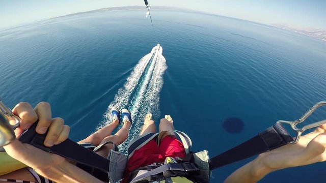 Parasailing over Adriatic sea young couple legs above crystal blue water point of view action camera