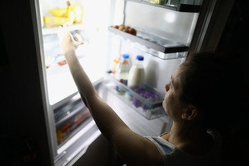 Woman at night opened refrigerator and takes out food portrait