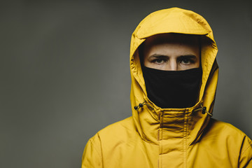 young skinny man wearing a yellow hooded jacket and black face mask with an aggressive serious look