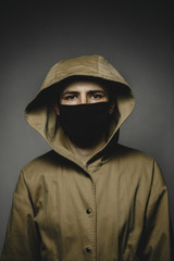 young skinny man wearing a yellow hooded jacket and black face mask with an aggressive serious look