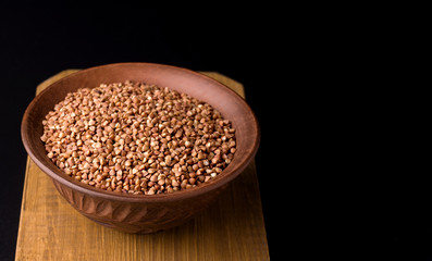 Buckwheat in a brown traditional bowl on a wooden board on a black background. Copy space. Banner