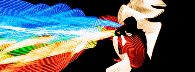 black silhouette of a man shooting a colorful, rainbow light with the camera in front of him. Dark background in the studio. Light painting technique.