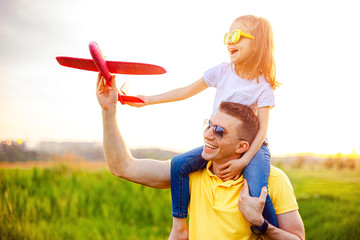 Cheerful man smiling and carrying excited girl on shoulders while playing with red aircraft...