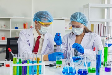 female and male scientist wear hairnet,safety glasses and mask testing chemical liquid in beaker and test tube in laboratory room