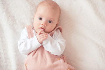 Small baby girl under 1 year old lying in bed over white in room closeup. Looking at camera. Childhood. Good morning.