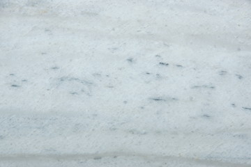 A polished slab of white marble with gray blurry stripes and dots called Nestos Beige