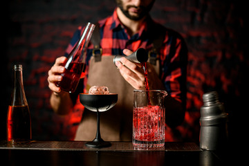 bartender pours red liquid from jigger into mixing cup