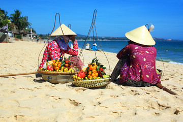 wietnamskie kobiety w tradycyjnych kapeluszach siedzące na plaży - obrazy, fototapety, plakaty