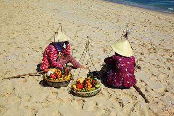 wietnamskie kobiety w tradycyjnych kapeluszach sprzedające owoce na plaży - obrazy, fototapety, plakaty