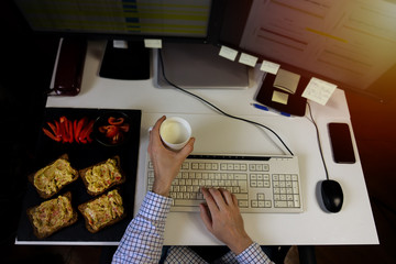 Busy business man eating healthy avocado toast breakfast while working on computer