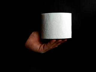 Männerhand hält eine Rolle weißes Toilettenpapier isoliert auf schwarzem Hintergrund