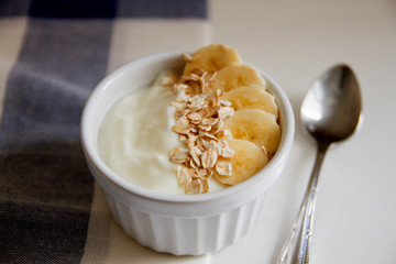 Healthy breakfast: yogurt with outmeal and banana in a white bowl on the table