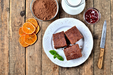 Gingerbread cakes, dried oranges, cacao powder, milk and jam on white plate and old knife. View from above.