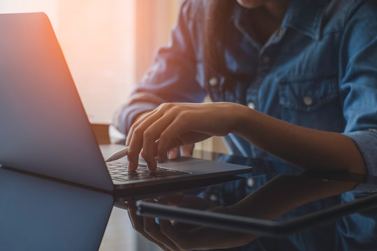Casual business woman hands holding electronic or stylus pencil and typing on laptop computer keyboard with black digital tablet on the desk at office. Online working concept. Flare light. - Powered by Adobe