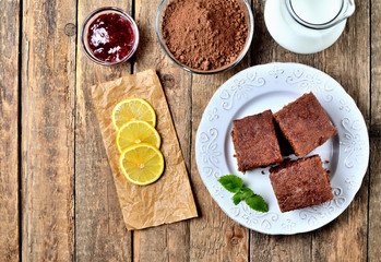 Gingerbread buns, dried pieces of lemon, cacao powder, milk and raspberry jam on white plate. View from above.