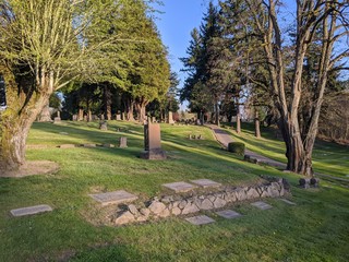 Graveyard at sunset, with trees, grave markers and a low stone ledge all visible in the foreground