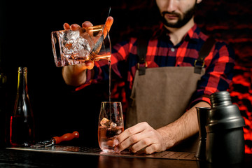 man at bar gently pours cold alcoholic cocktail r into glass