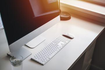 Home office theme. Computer, keyboard, mouse and glass of water on white table.