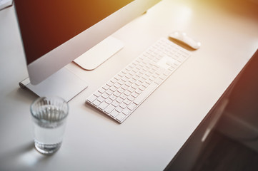 Home office theme. Computer, keyboard, mouse and glass of water on white table.