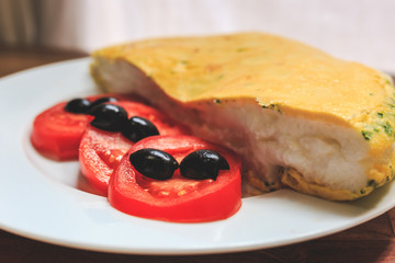 A very puffy omelet with greens and cheese inside and tomatoes and olives on the side in a white...