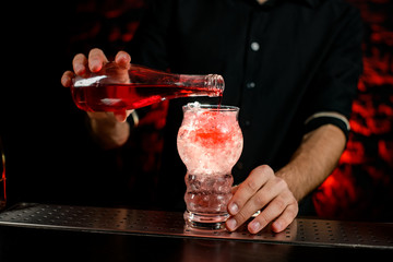 Close-up bartender pouring drink to glass full of pieces of ice.