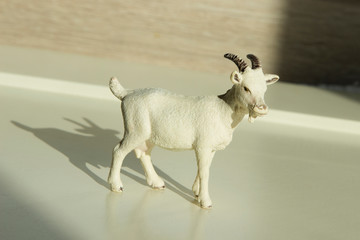 very small toy plastic kid, goatling with shadow on a wooden table