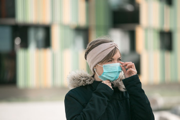 Fototapeta premium Flue and corona safety concept. Woman putting on face mask to protect herself, outdoors