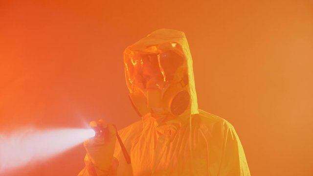 Man in a yellow protective suit shines a flashlight in the smoke. Apocalypse. Lifeguard in chemical suit with respirator and goggles.