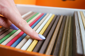 A young woman runs her finger through the samples of colored furniture panels when choosing. Panel...