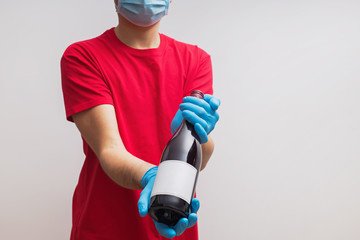 Delivery man wearing protective gloves and mask holding a bottle of wine