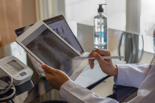Female doctor hand holding digital tablet with chest x-ray film (CXR ) on screen and work on laptop computer at the office in clinic or hospital. Medical and health care concept.