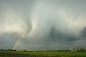 Bright colorful rainbow caused by a spectacular shower with rain and hail streaks over the transylvanian landscape