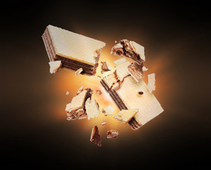 Chocolate waffles crushed into pieces in the air with flash of light in the dark