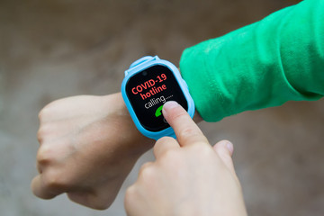 little boy calls in COVID-19 hotline on digital smart watch by tapping screen with his index...