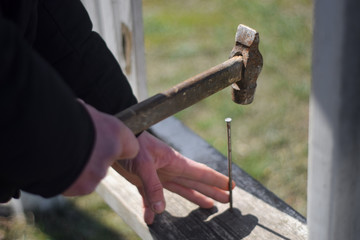 Worker hammer a nail into a wooden board. Old hammer in hand close up. Hammer in hand of engineer or handyman. Hand tool close up