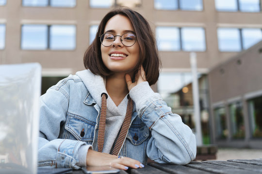 Close-up Portrait Of Young Attractive Queer Girl In Denim Jacket, Student Sitting Outside With Laptop, Smiling At Camera With Pleased Calm Expression, Have A Break From Work On Project