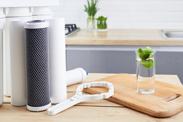 A glass of clean water and filter cartridges on the home kitchen background