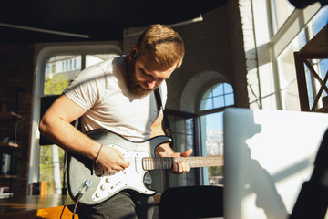 Caucasian musician playing guitar during online concert at home isolated and quarantined. Using camera, laptop, streaming, recording courses. Concept of art, support, music, hobby, education.