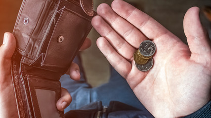 man holds an empty wallet in his left hand and a few coins in his right hand. concept of economic crisis. low salary . Russian rubles .