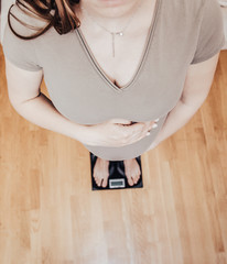 Pregnant woman standing on scales at home, closeup. Pregnant lady measuring her weight, taken from...