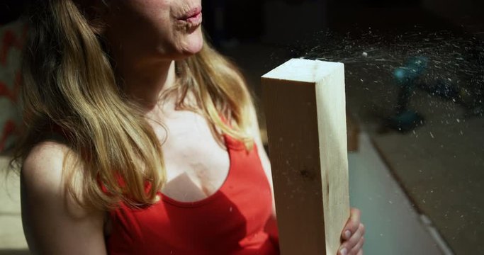 Young woman blowing sawdust from wooden post she has cut