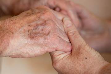 Ein Frau mittleren Aters hält die Hände eines über 80 jährigen Mannes