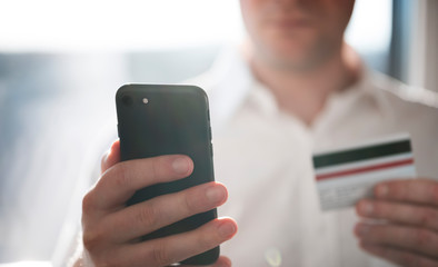 Close-up of a businessman using a smartphone for paying cashless, holding a credit card in the other hand