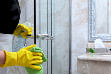 The doors in the shower stall are washed with a napkin. Cleaning at the hotel or at home. Unrecognizable photo. The concept of cleanliness and hygiene.