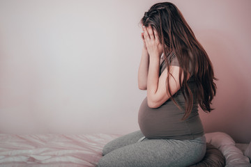 Sad woman crying while sitting on bed in her bedroom. Stressed pregnant woman or mother problems.