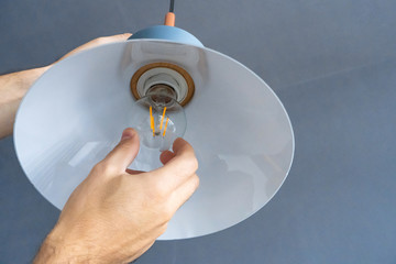 Close-up. A hand changes a light bulb in a stylish loft lamp. Spiral filament lamp. Modern interior...